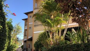 A multi-story building with a beige facade, surrounded by lush greenery and palm trees. - Pousada Gênesis (Arraial do Cabo)