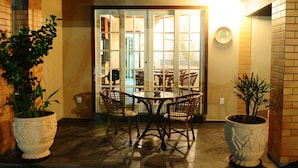 A dining area with a round table and four wicker chairs, surrounded by potted plants. - Pousada Gênesis (Arraial do Cabo)