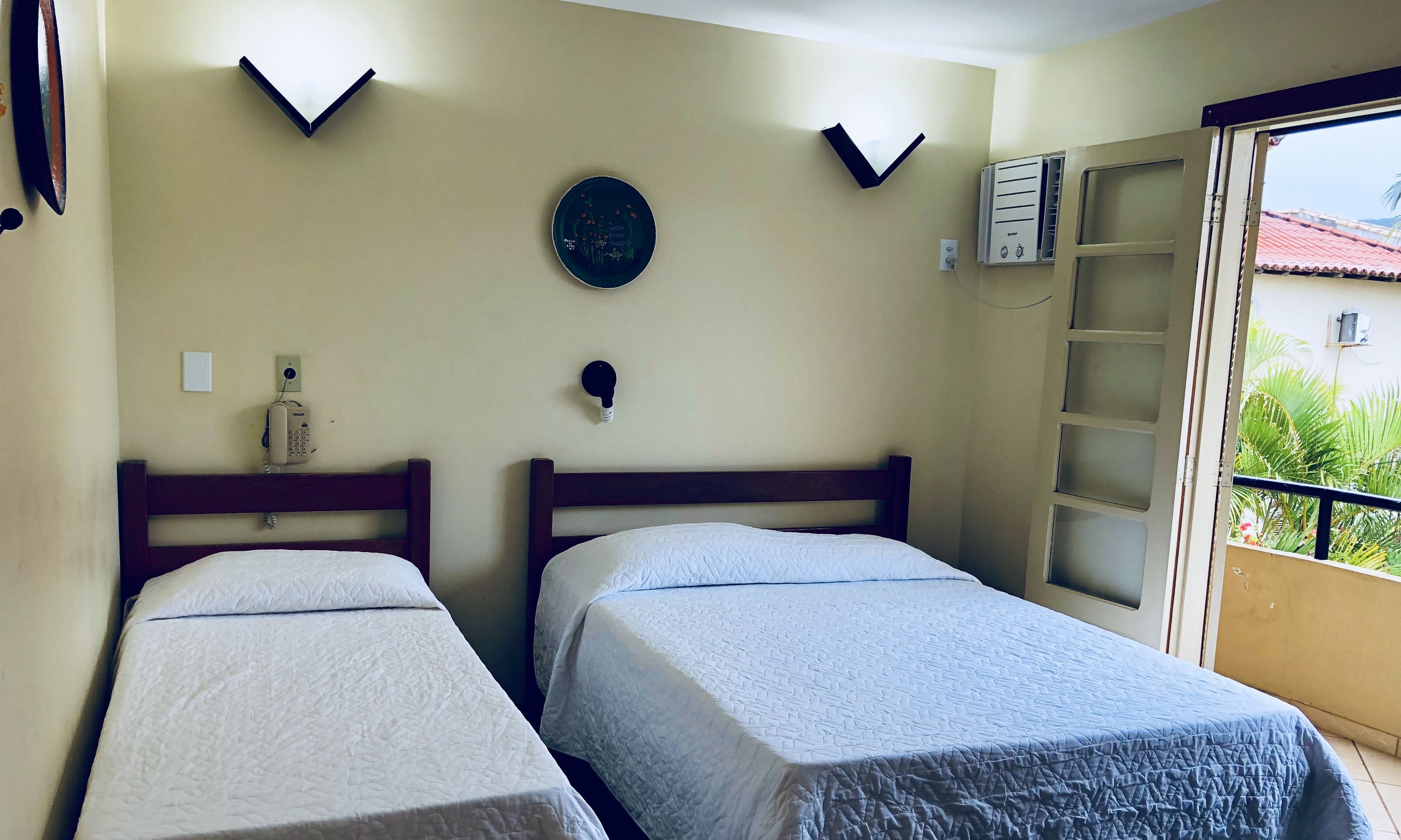A room with two beds, a wall-mounted light fixture, a plate, and an air conditioning unit.
