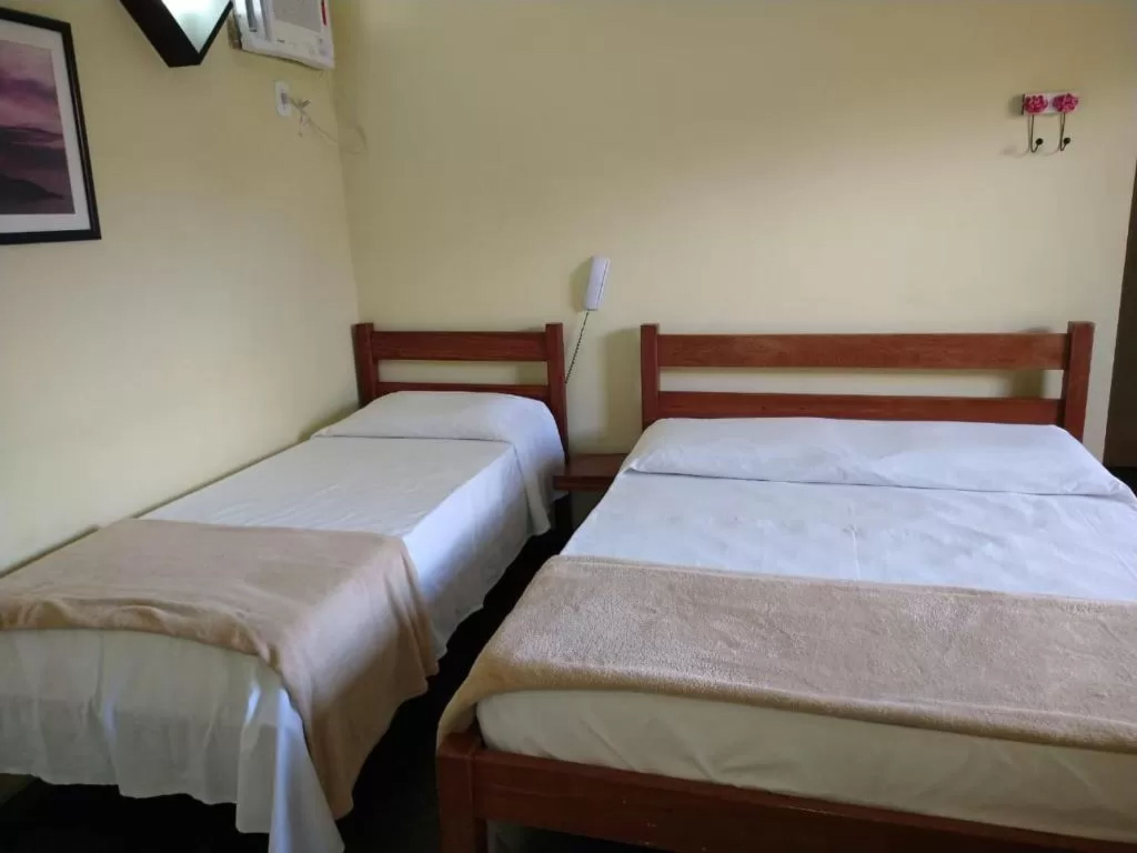 Une chambre avec deux lits simples, une table de chevet, un téléphone fixé au mur et un tableau encadré.