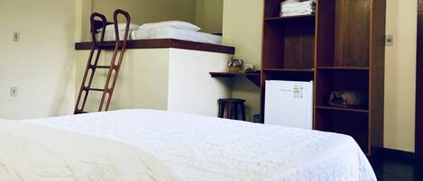 Habitación de hotel con cama, escalera de madera, refrigerador y estante de madera con toallas dobladas.