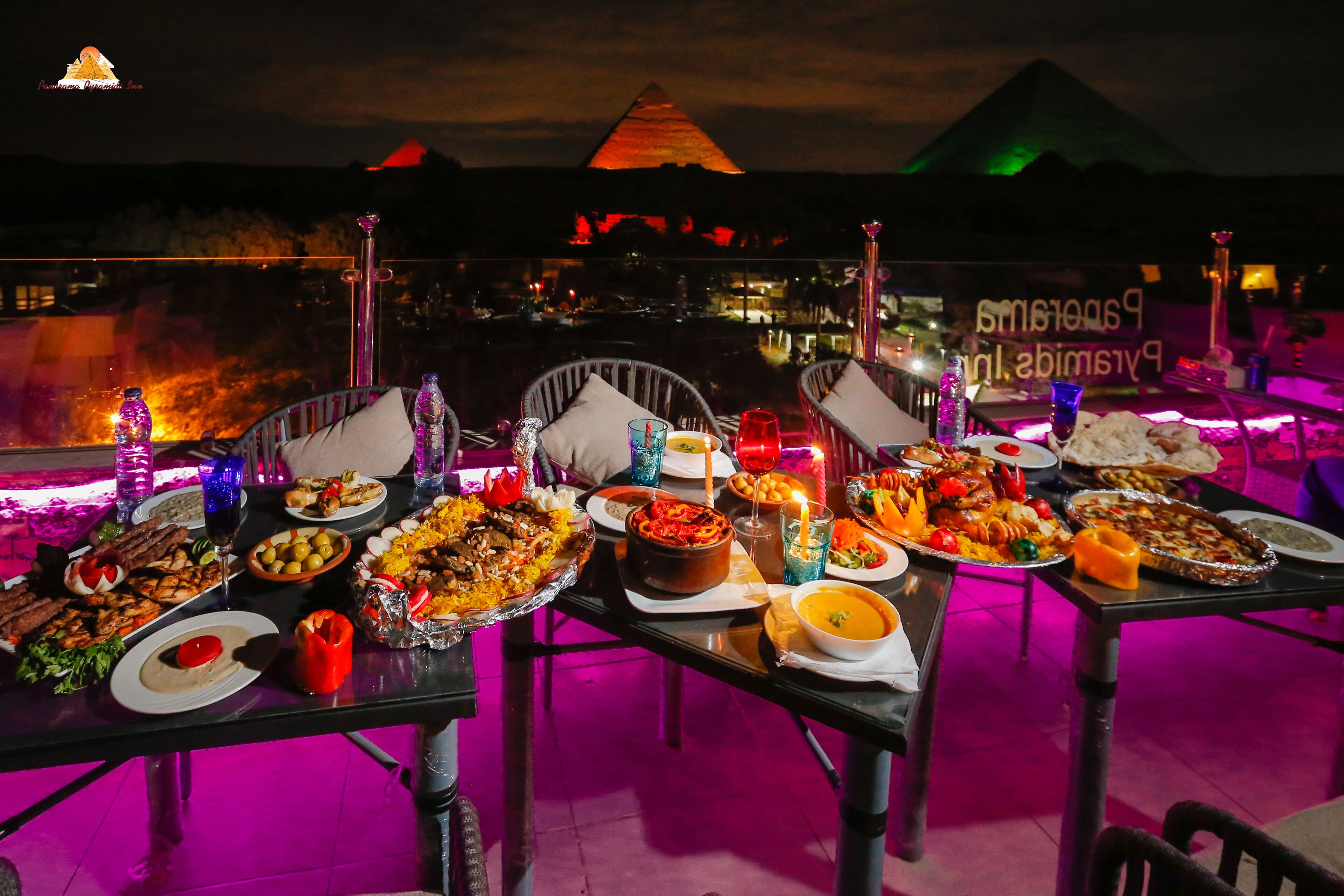A table set for a meal with various dishes, a view of the pyramid, and a sign with text.