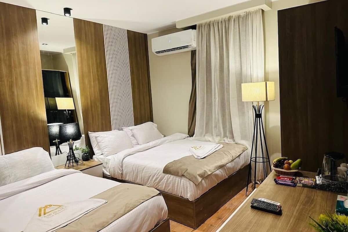 Habitació d'hotel amb dos llits, una taula de nit amb làmpada, una cafetera i un plat de fruita.