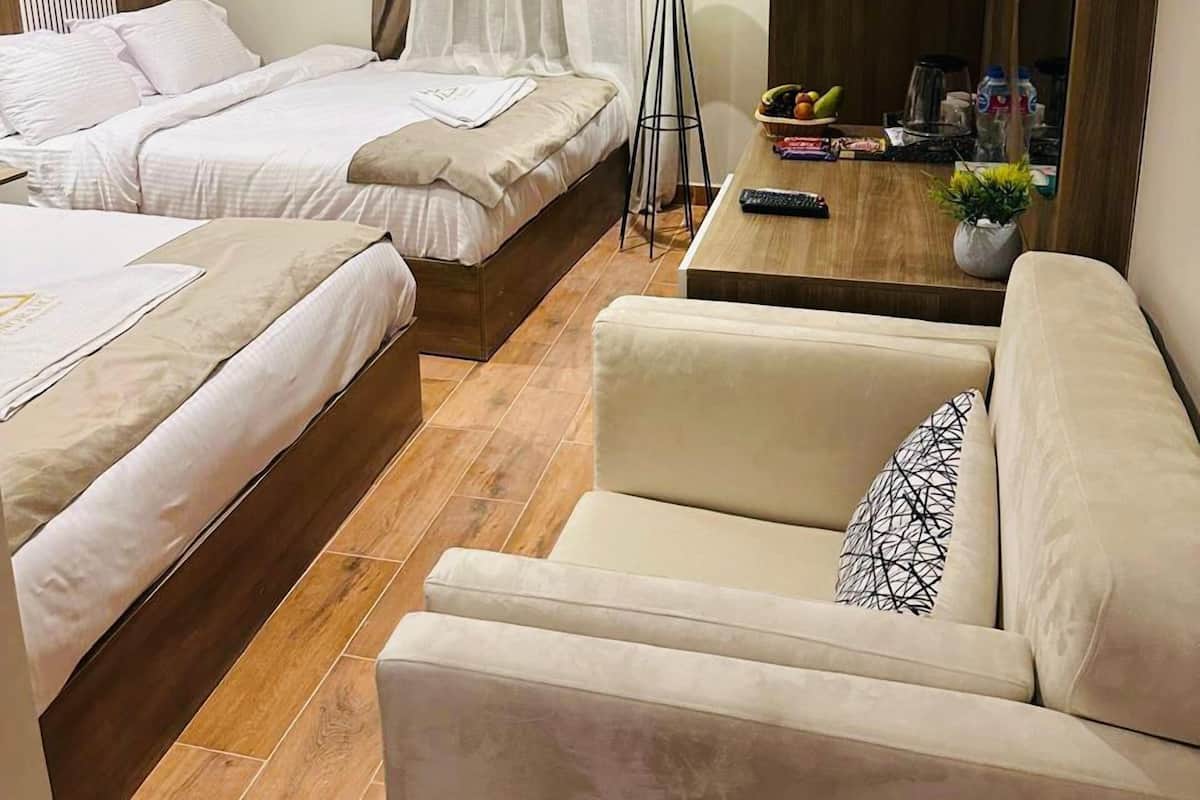 Habitació d'hotel amb dos llits, un sofà, una taula de café, una làmpada i un televisor.