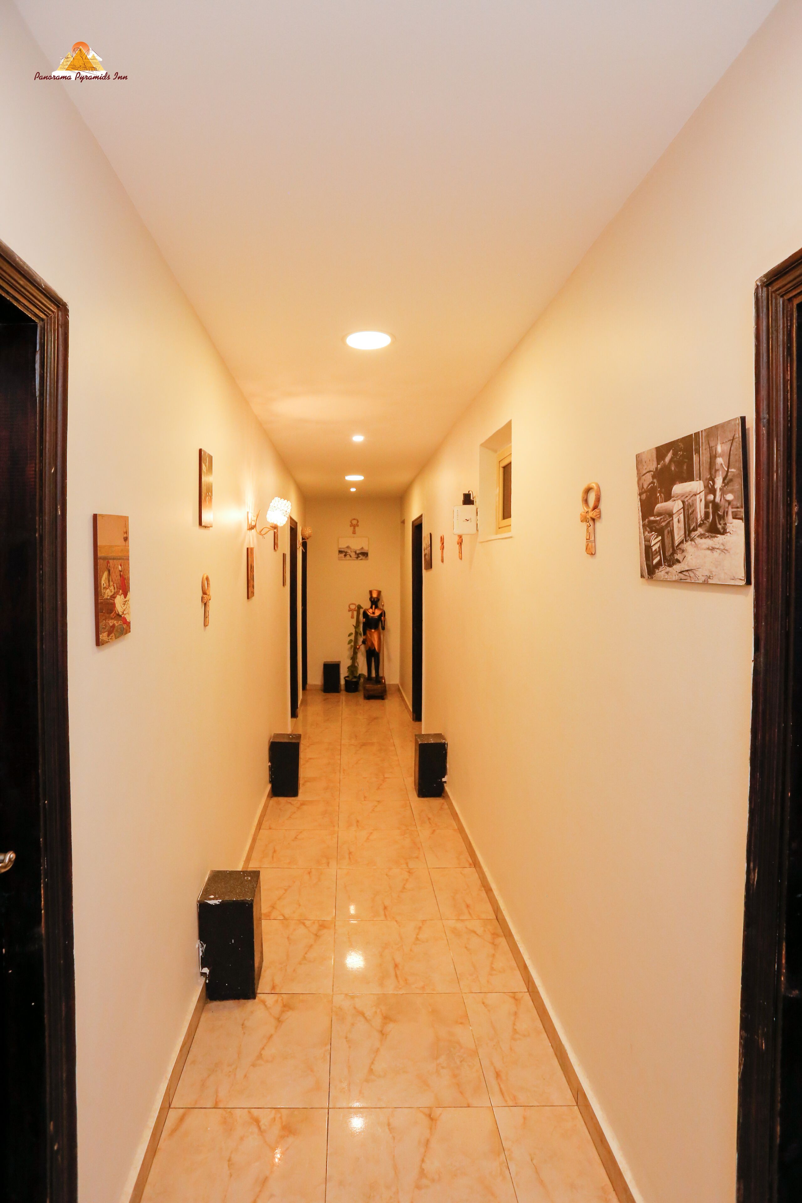 A hotel hallway with marble flooring, framed artwork on the walls, and a statue in the distance.