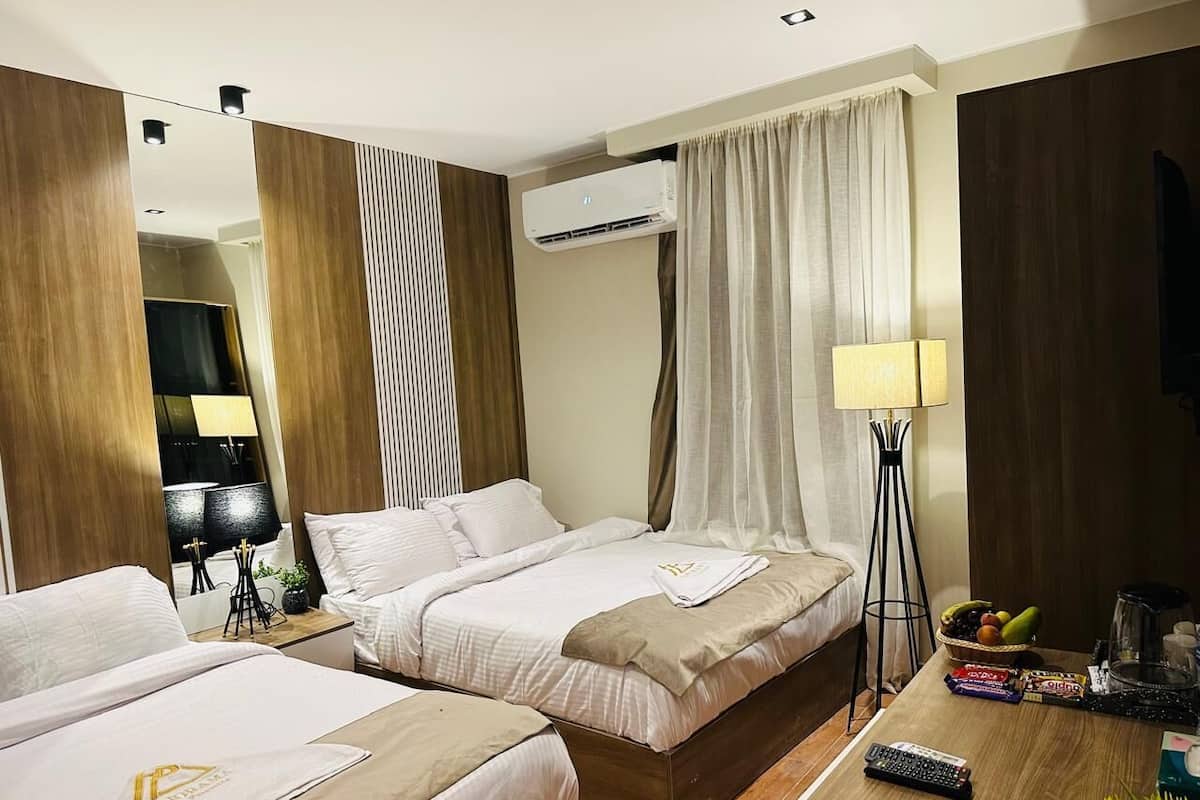 Habitació d'hotel amb dos llits, una taula de nit amb una làmpada, una taula de cafeteria amb aperitius i un aparell d'aire condicionat.