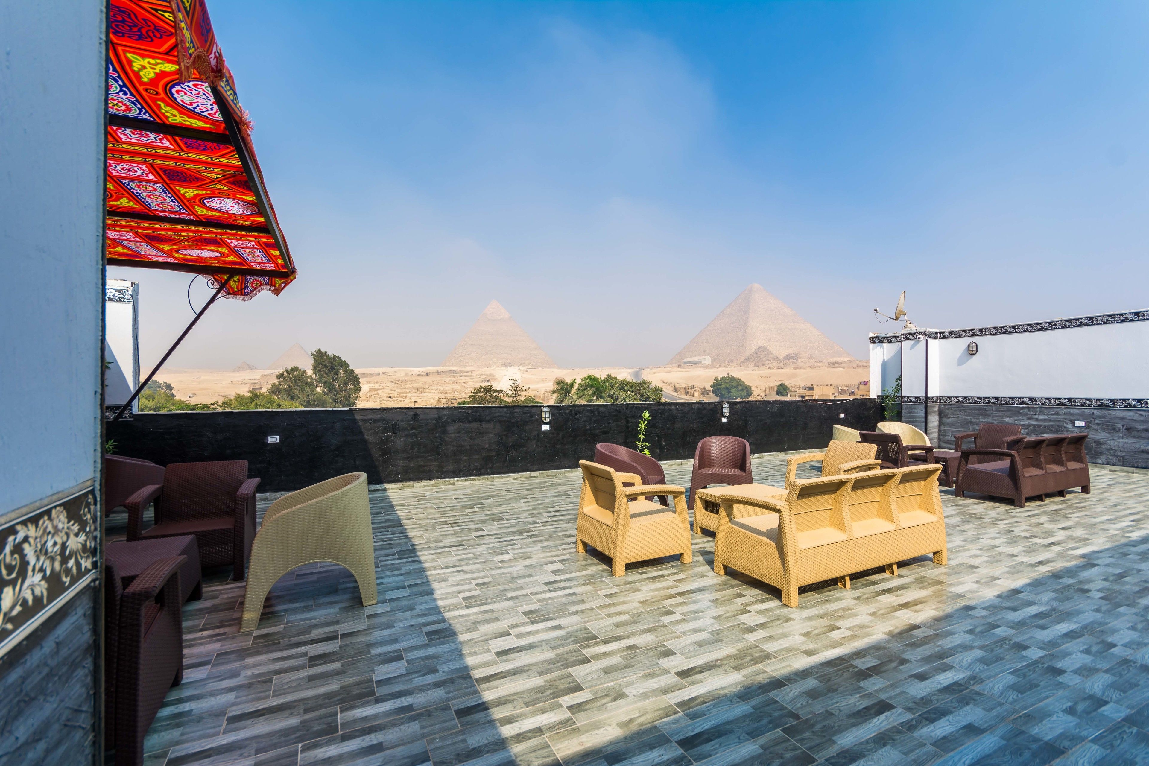 A rooftop terrace with wicker furniture and a view of the pyramids.