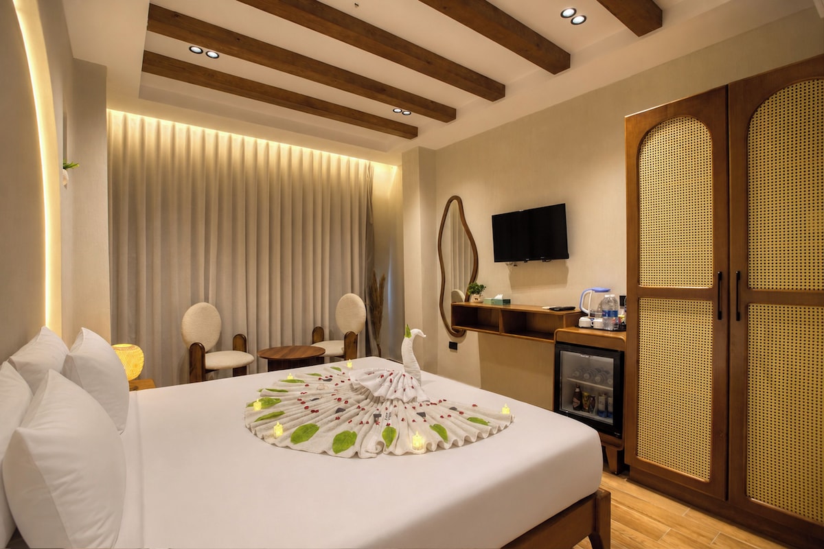 A hotel room with a large bed, a flat-screen TV, a minibar, and a wooden wardrobe.