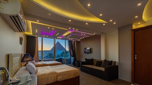 A hotel room with a bed, a sofa, a TV, and a view of a pyramid.