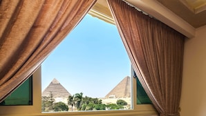 A room with a view of the pyramids, a table with breakfast items, and two chairs.