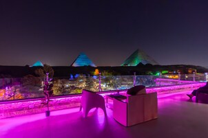 Terraza en la azotea con asientos y vistas a pirámides iluminadas.