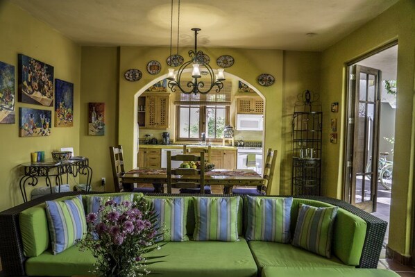 Un salon chaleureux avec un canapé vert, une table à manger et une cuisine en arrière-plan.
