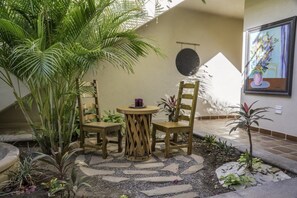 Un espace patio avec une table ronde et quatre chaises en bois, entouré de plantes en pot et d’un petit jardin.