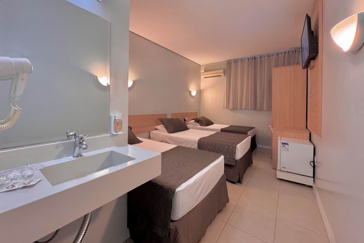 A hotel room with a bathroom, two beds, a TV, and a small refrigerator.