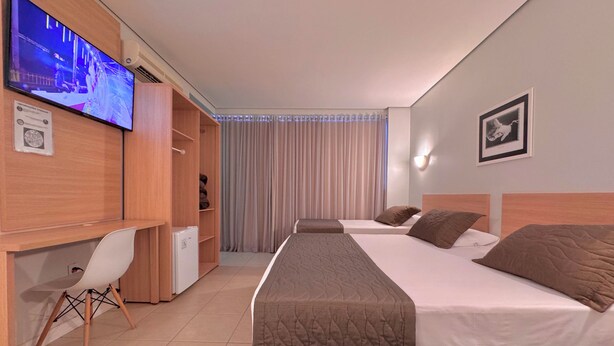Habitación de hotel con dos camas, un escritorio, una silla, un televisor y una cortina.