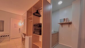Una habitación con armario, escritorio, refrigerador, estante con objetos y zona de cocina.