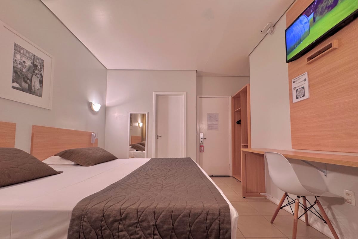 A hotel room with a bed, a desk, a chair, a television, and a mirror.