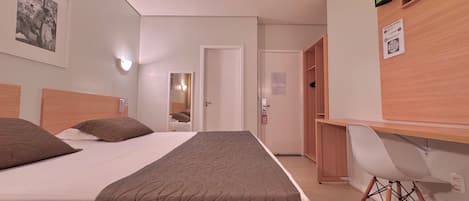 Una habitación de hotel con cama, escritorio, silla, televisor y espejo.