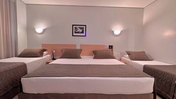 Quarto de hotel com uma cama grande, duas camas menores, cabeceira com telefone, luminárias fixadas na parede e um quadro emoldurado.