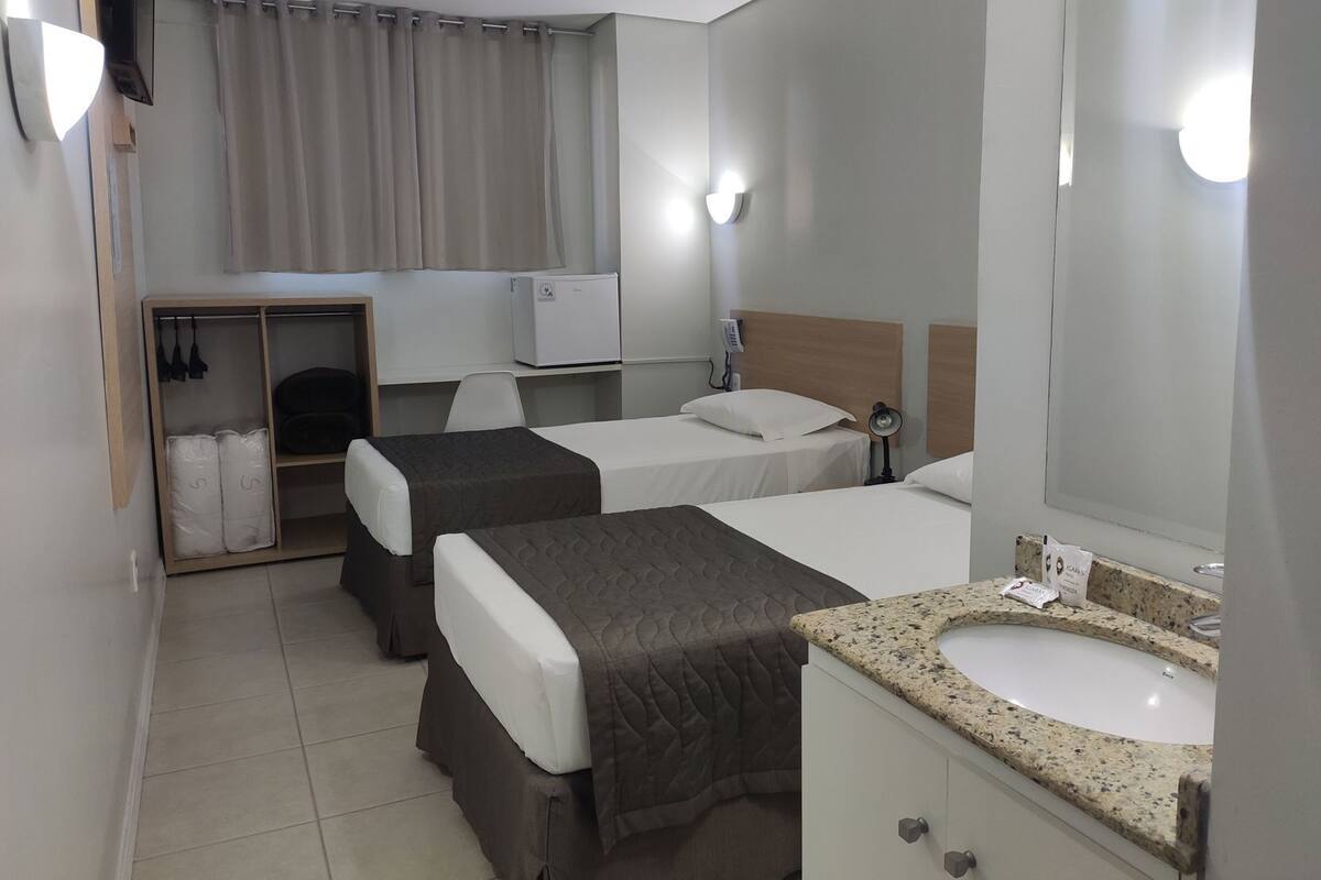 A hotel room with two beds, a TV, a desk, a wardrobe, and a bathroom with a sink and mirror.