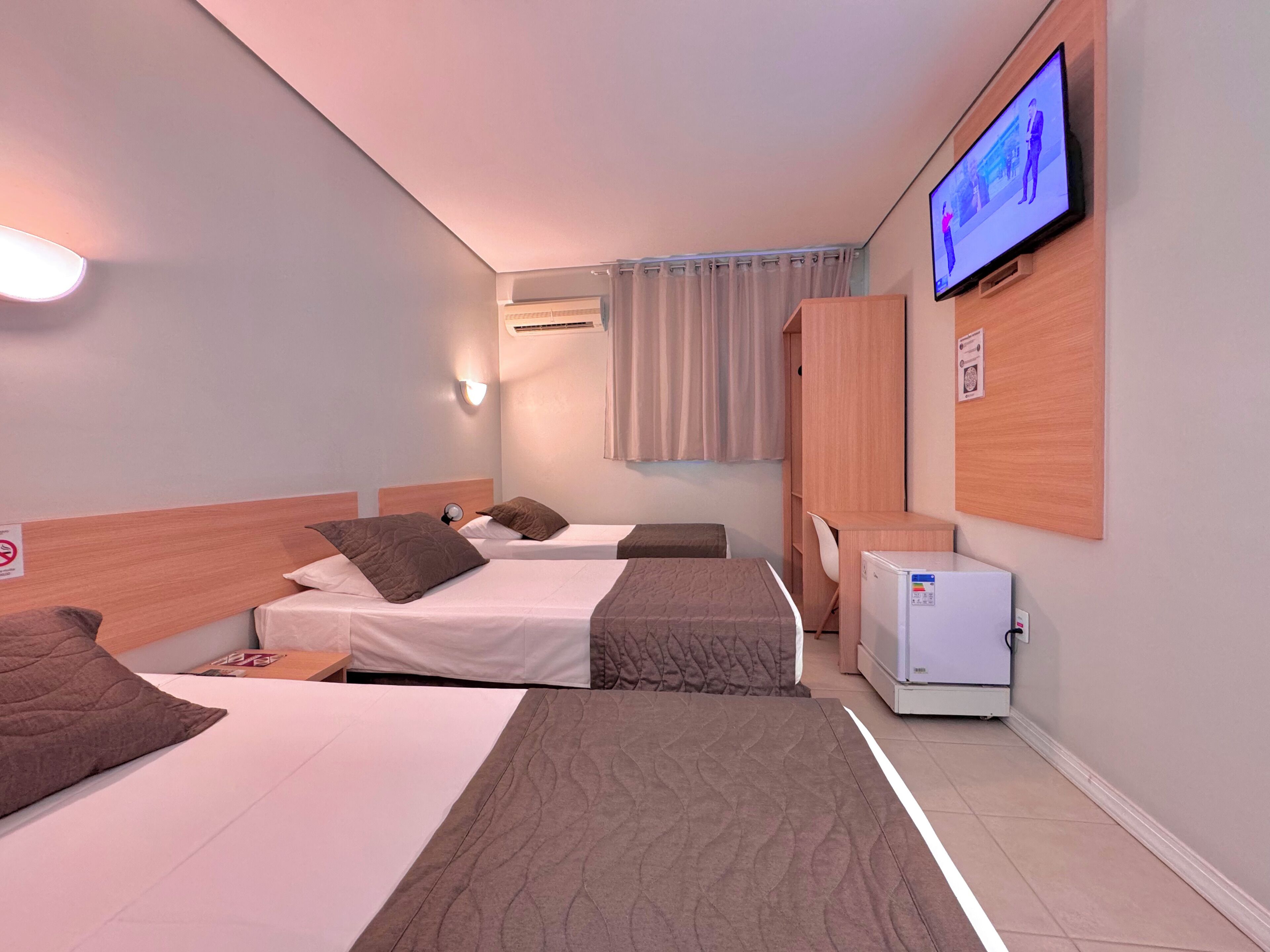 A hotel room with two beds, a TV, a desk, and a refrigerator.