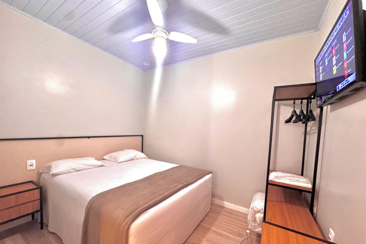 A bedroom with a bed, a ceiling fan, a TV mounted on the wall, and a shoe rack.