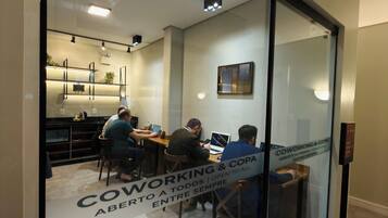 A modern office space with glass partitions, a kitchen area, and a sign indicating coworking and open to all.
