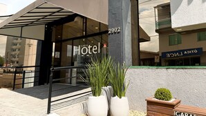 Entrada de un hotel con diseño moderno, que incluye fachada de vidrio y marquesina metálica.