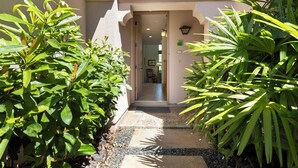 A narrow pathway leading to a building entrance, flanked by lush green plants. - Walk to Golf 250' from your door. Swim, Play, Feel the Warmth of Caring Owner (Waikoloa)
