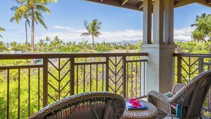 A covered outdoor seating area with wicker furniture, a view of palm trees, and a clear sky. - Walk to Golf 250' from your door. Swim, Play, Feel the Warmth of Caring Owner (Waikoloa)