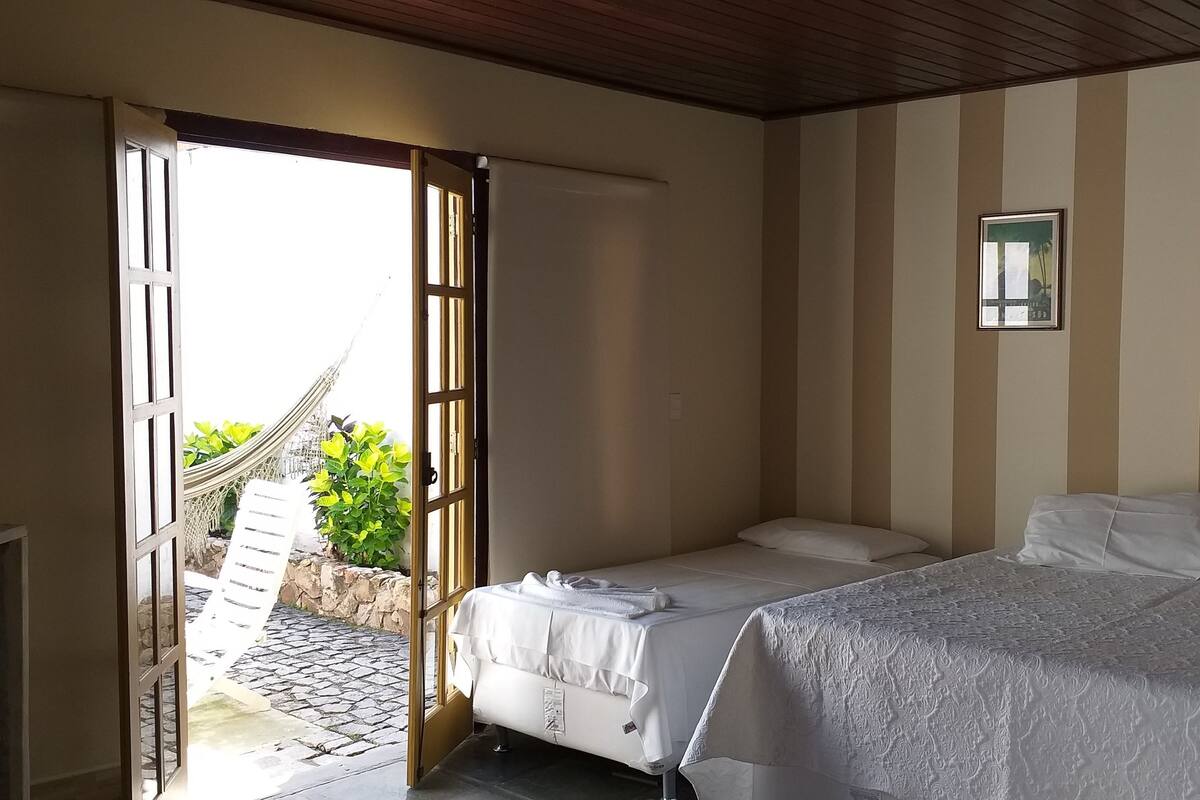 Habitación de hotel con cama, televisión, una hamaca frente a la puerta y vista a zonas verdes.