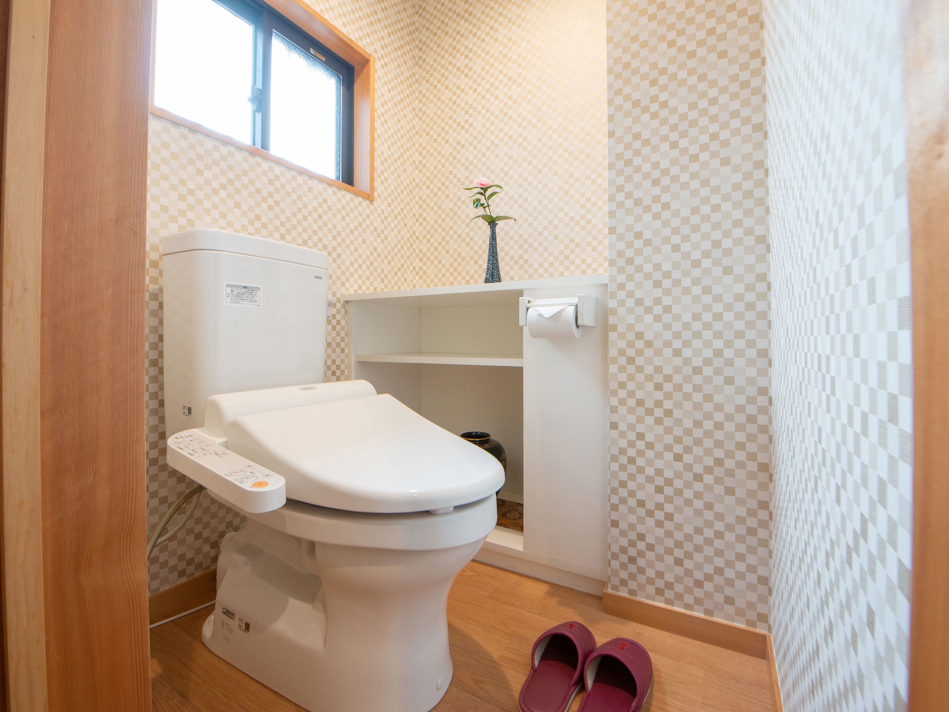 A modern bathroom with a toilet, a small shelf with a vase, and a pair of slippers on the floor.