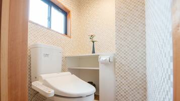 A modern bathroom with a toilet, a small shelf with a vase, and a pair of slippers on the floor.