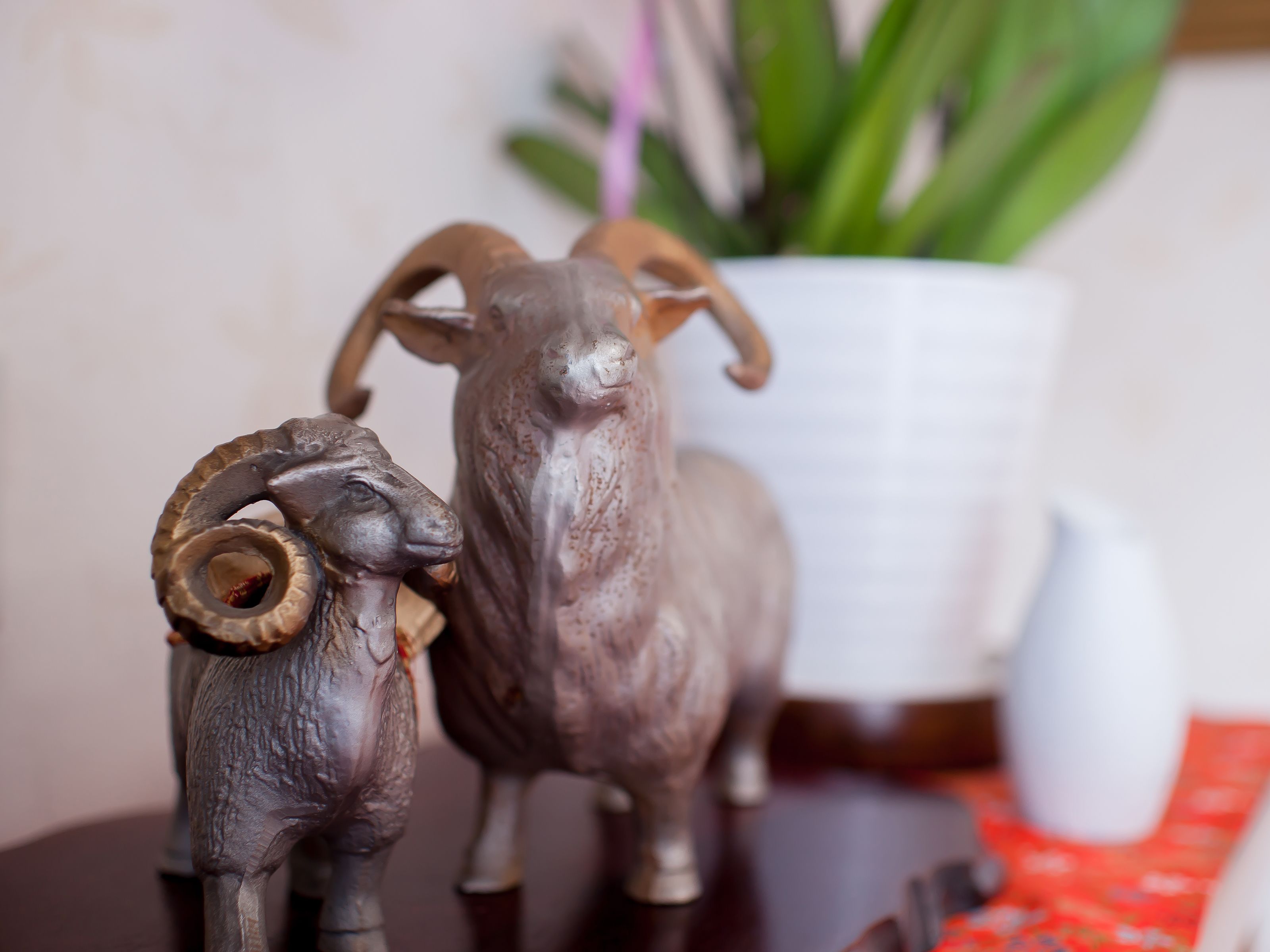 Two goat figurines on a table with a white mug and a green plant in the background.