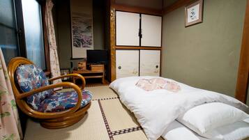 A traditional Japanese-style room with tatami flooring, a futon bed, a wooden rocking chair, and a television on a low shelf.