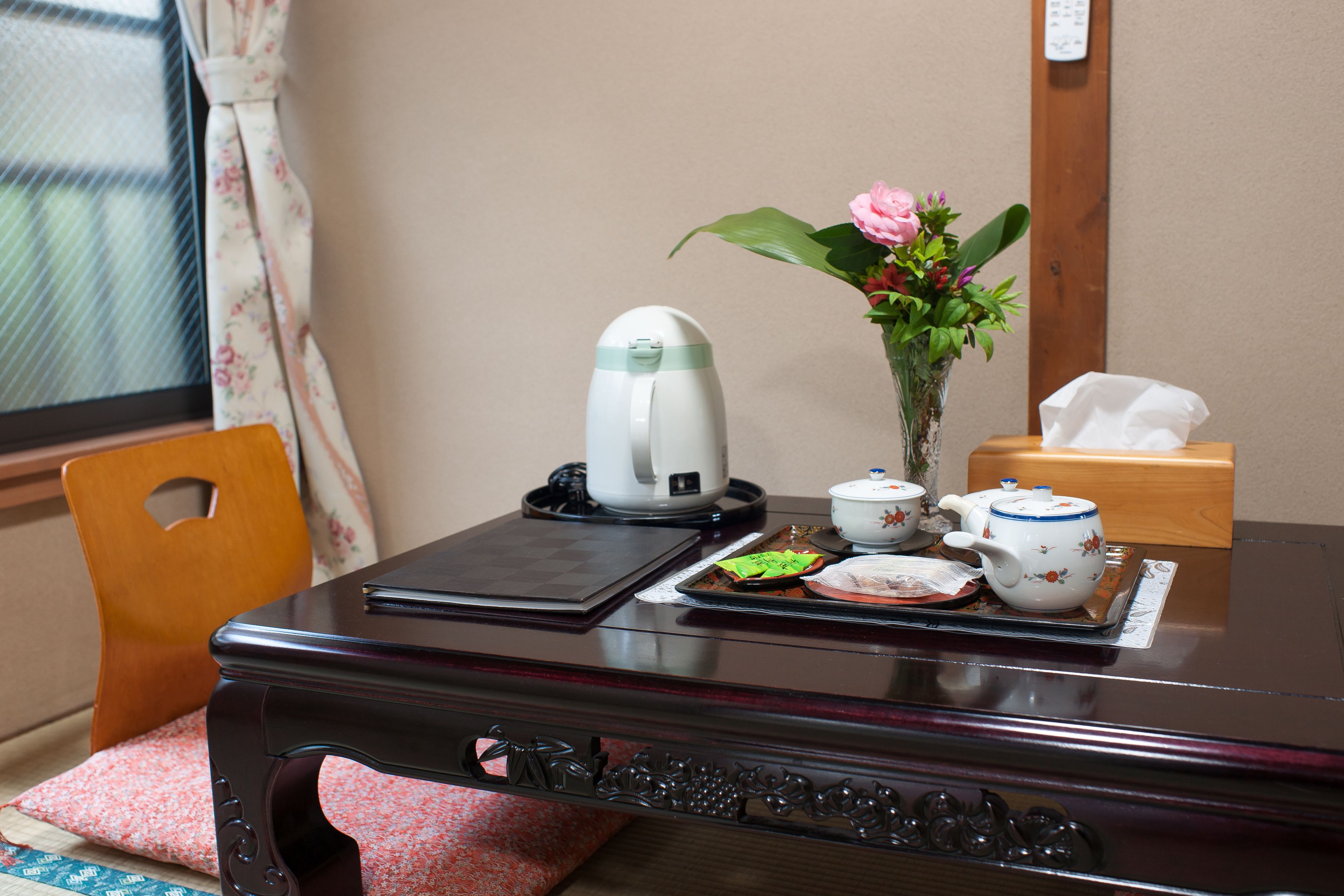 A wooden desk with a tea set, a vase with flowers, and a tissue box.