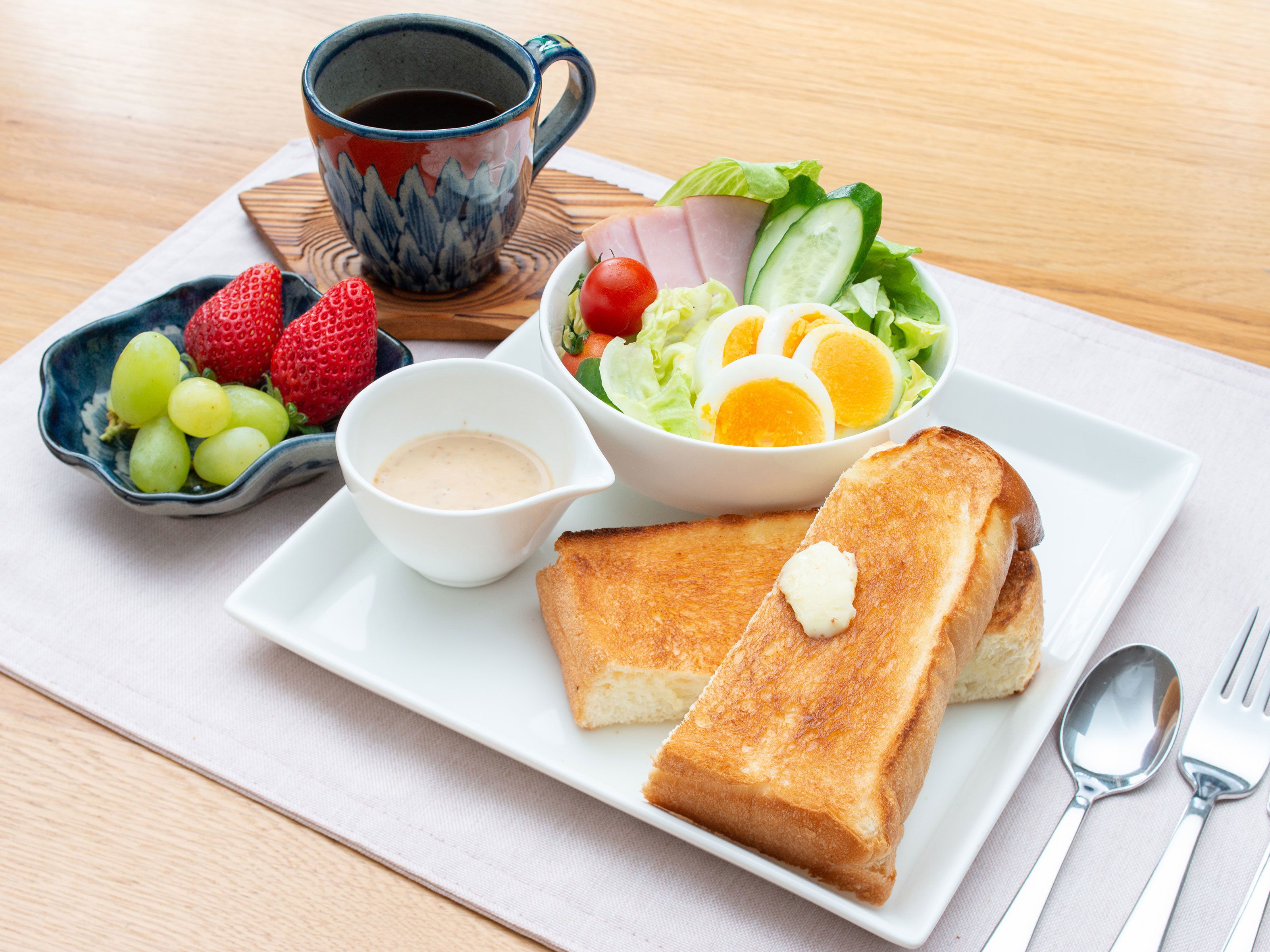 Ein Teller mit Toast, eine Salatschüssel, eine Kaffeetasse und eine Schale Obst.