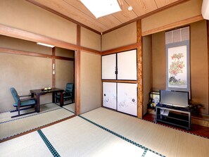 A traditional Japanese room with tatami flooring, a low table with chairs, a sliding door, and a television on a stand.