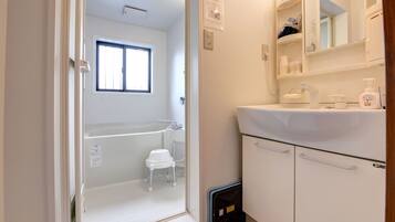 A bathroom with a bathtub, a sink, and a mirror. There is a window above the bathtub and a small stool near it.