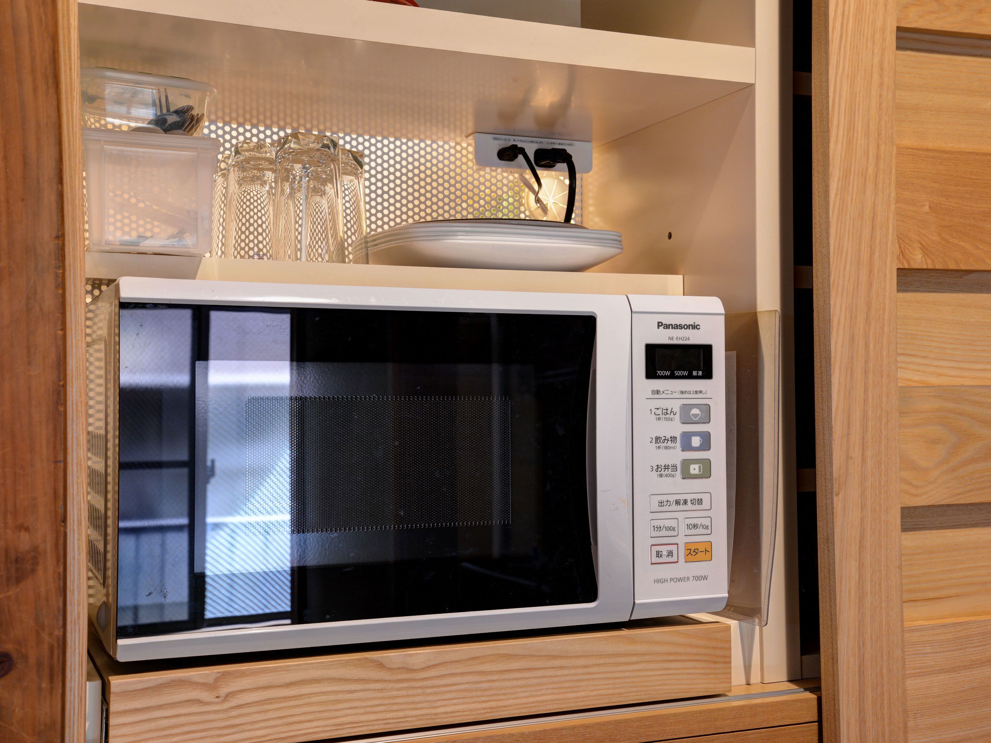 A Panasonic microwave oven with a digital display, placed on a wooden cabinet.
