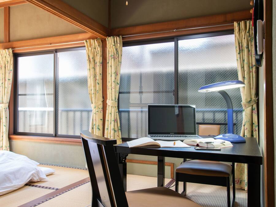 Habitació amb un llit, un escriptori, un ordinador portàtil, una cadira i una làmpada de taula.