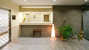 A reception area with a 'FRONT' sign, a clock, a small table, a potted plant, and a dog statue. - Koga Central Hotel (Koga)