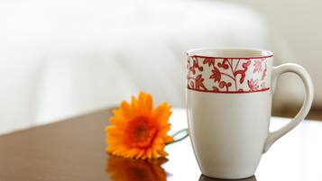 A white mug with a red floral pattern and a single orange flower beside it.