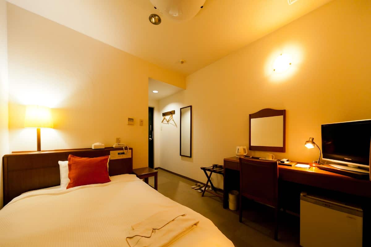 Una habitación de hotel con cama, escritorio, silla, televisión y un refrigerador pequeño.