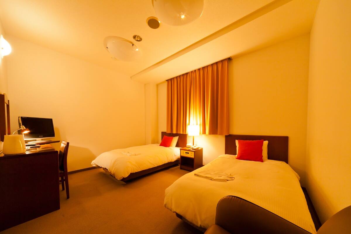 Una habitación de hotel con dos camas, un escritorio, una computadora, una lámpara y una silla.