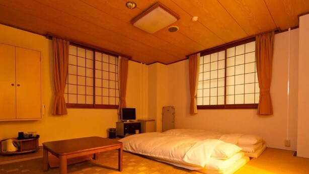 A traditional Japanese-style room with tatami flooring, a futon bed, a wooden table, and sliding doors with shoji screens. - Koga Central Hotel (Koga)