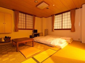 A traditional Japanese-style room with tatami flooring, a futon bed, a wooden table, and sliding doors with shoji screens. - Koga Central Hotel (Koga)