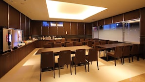A conference room with a long table and chairs, a kitchen area with appliances, and a large screen for presentations.