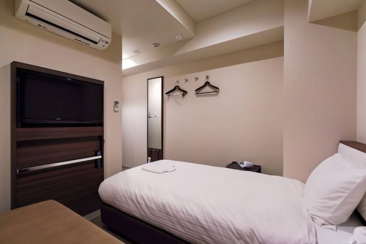 A hotel room with a bed, a TV mounted on the wall, a mirror, and a coat rack.