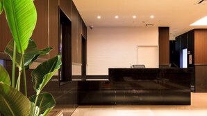 A modern reception area with a black reception desk, a large potted plant, and a textured wall.